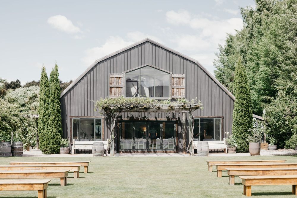 Rustic barn wedding venue with wooden benches arranged for outdoor ceremony on sunny day.