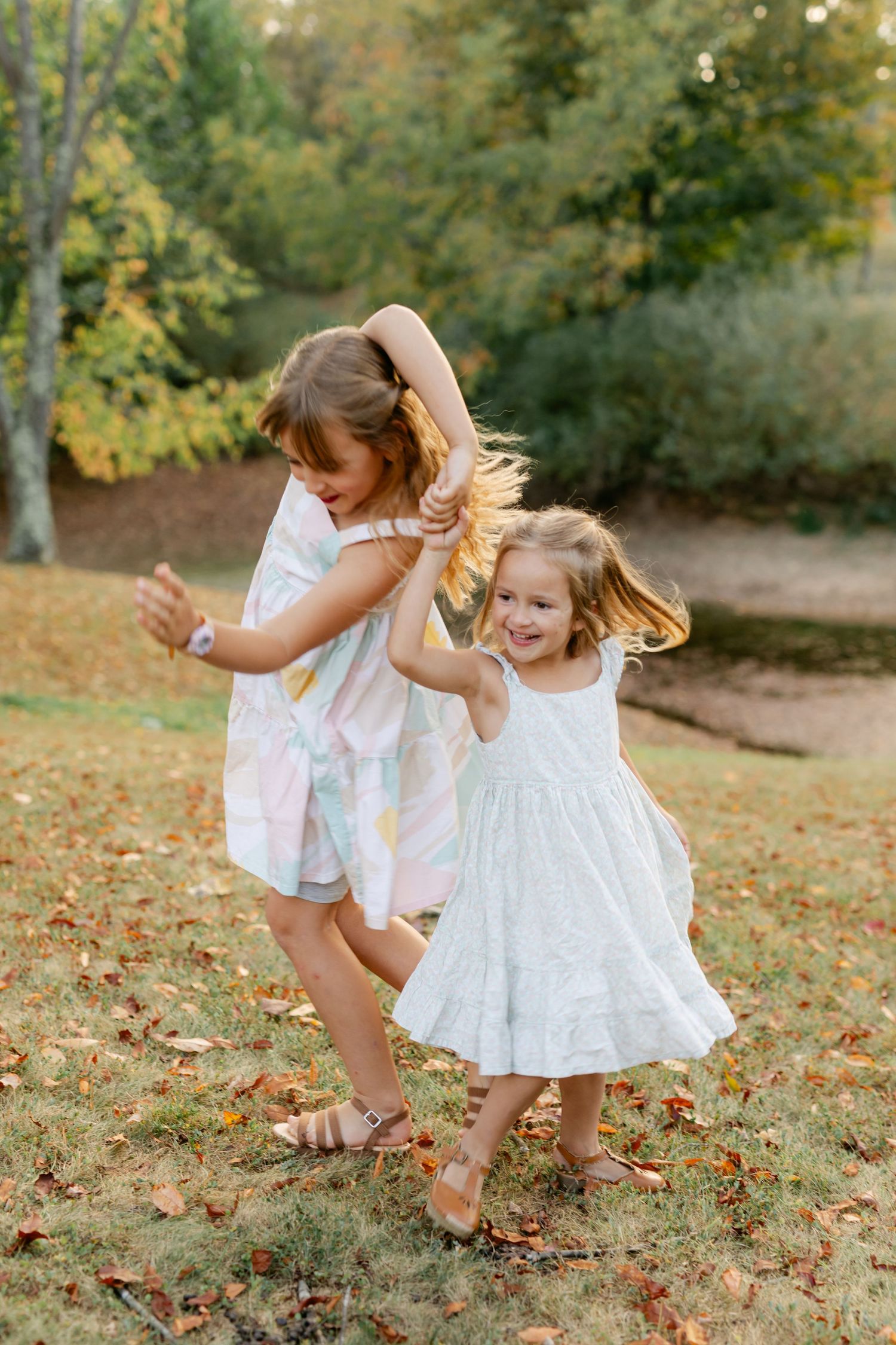 Two young girls in summer dresses dancing and playing together in autumn park.