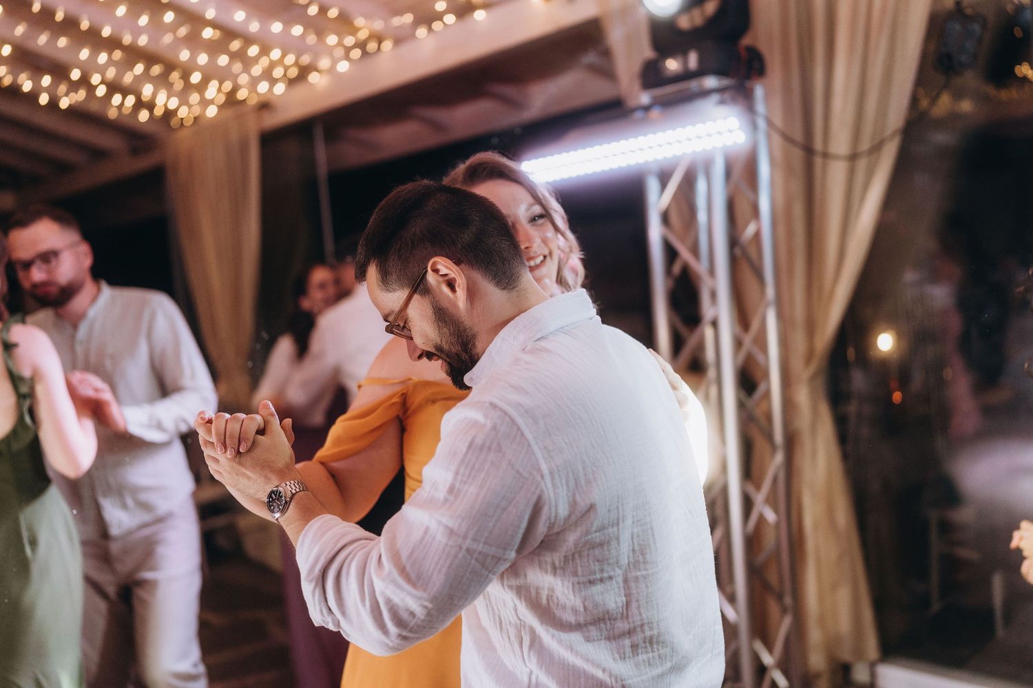 Couple sharing a romantic dance at wedding reception under warm string lights at evening celebration.