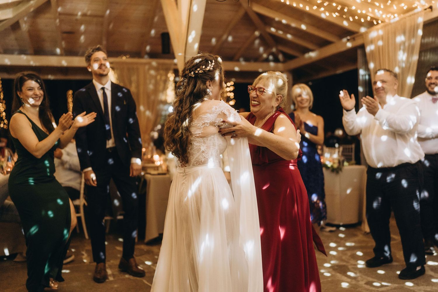 Bride dances joyfully with a guest in a red dress at a rustic barn wedding reception with confetti.