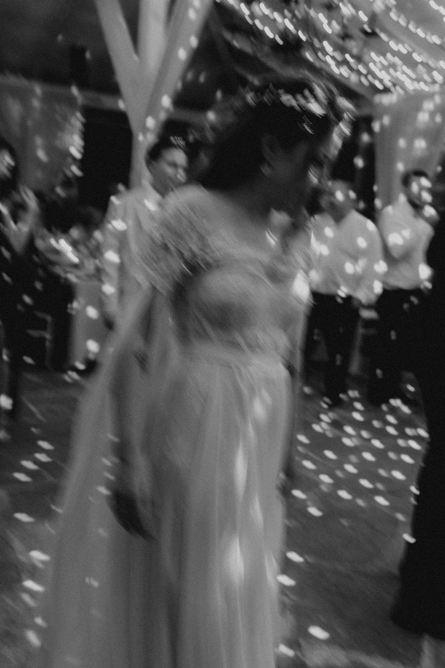 Blurred black and white artistic photo of bride walking through confetti shower at elegant wedding reception.