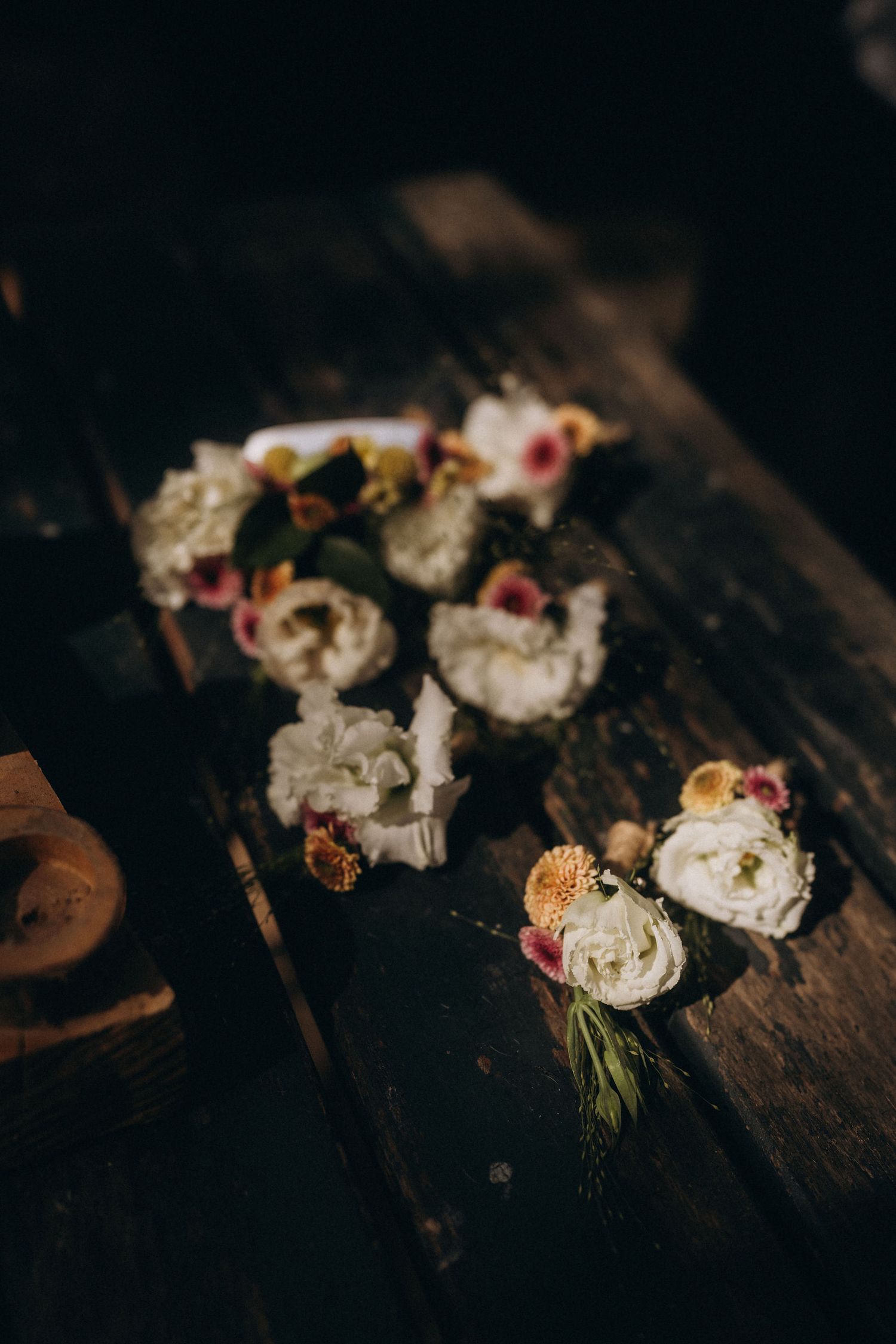 White and pink flowers arranged on a rustic wooden table in a moody, dark floral display.