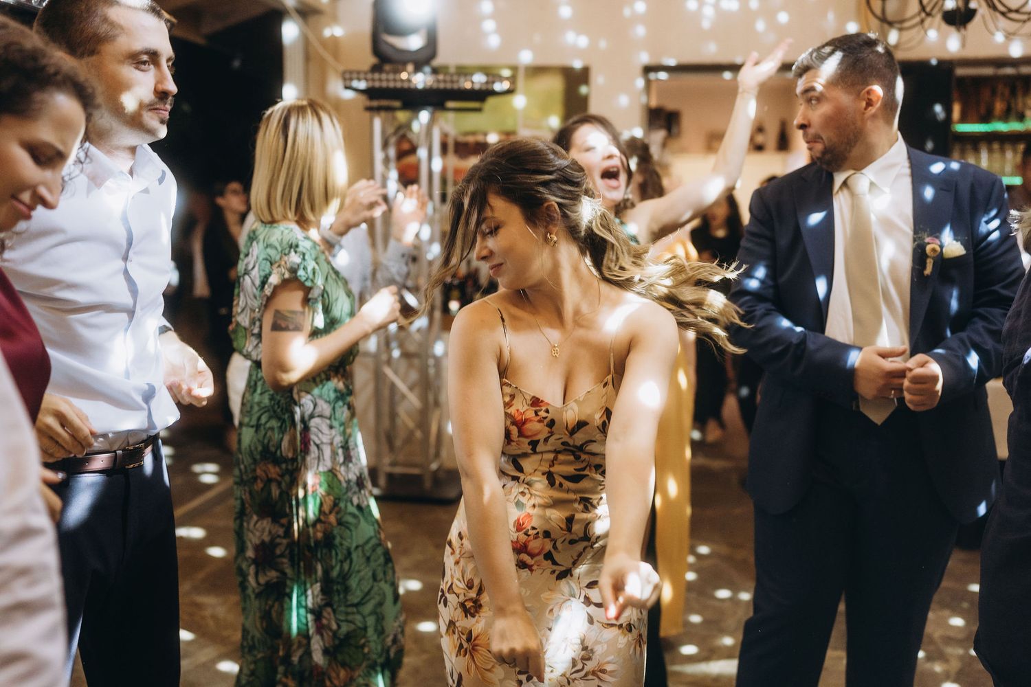 Woman in floral dress dancing joyfully with guests at elegant wedding reception party.
