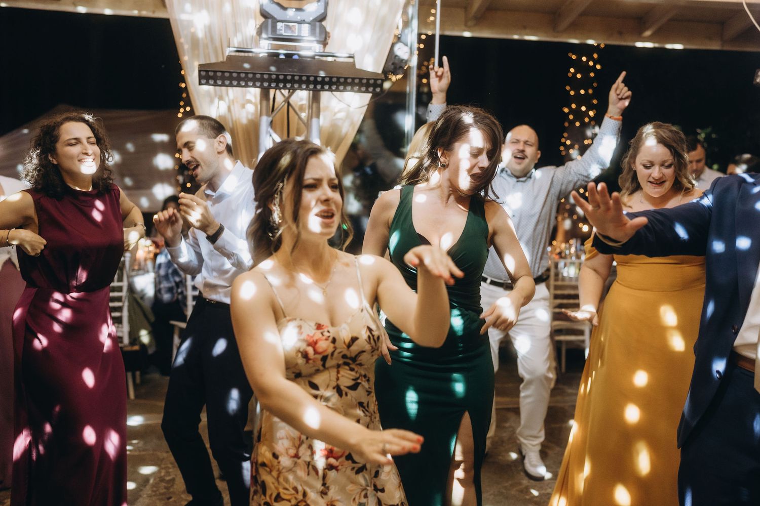 Guests dancing and celebrating at a festive wedding reception with string lights and colorful confetti.