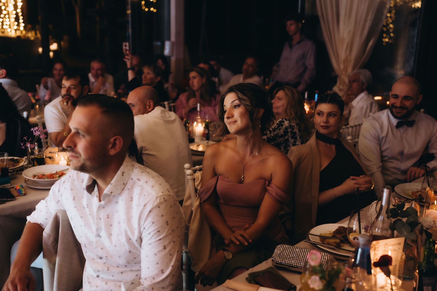 Wedding guests seated at candlelit reception dinner table enjoying the evening celebration.