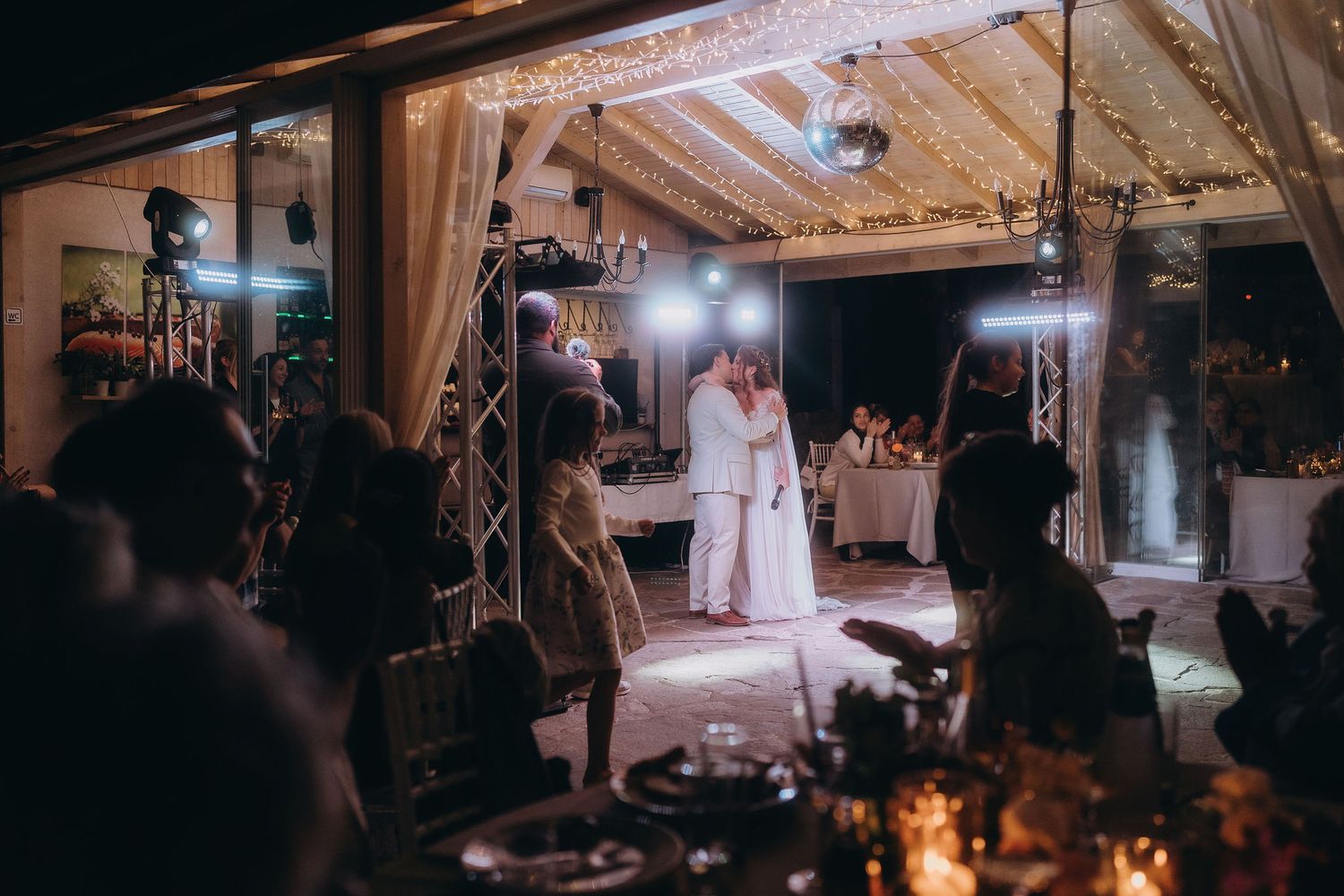 Bride and groom share first dance under elegant string lights at romantic outdoor wedding reception at night.