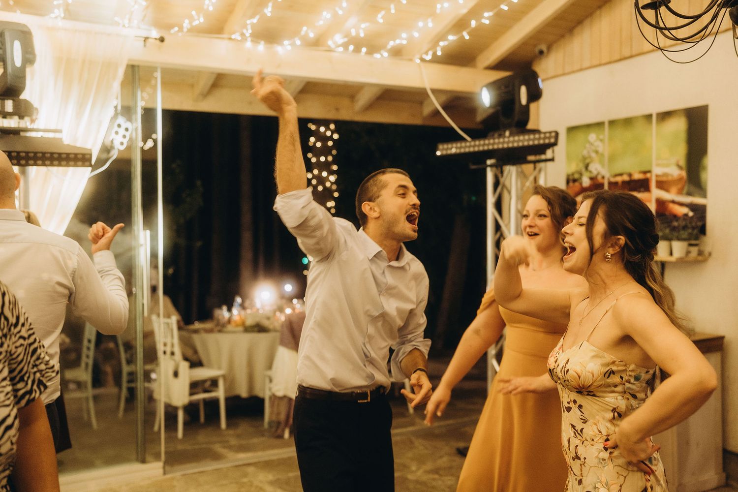 Joyful wedding guests laugh and celebrate on the dance floor during lively evening reception party.
