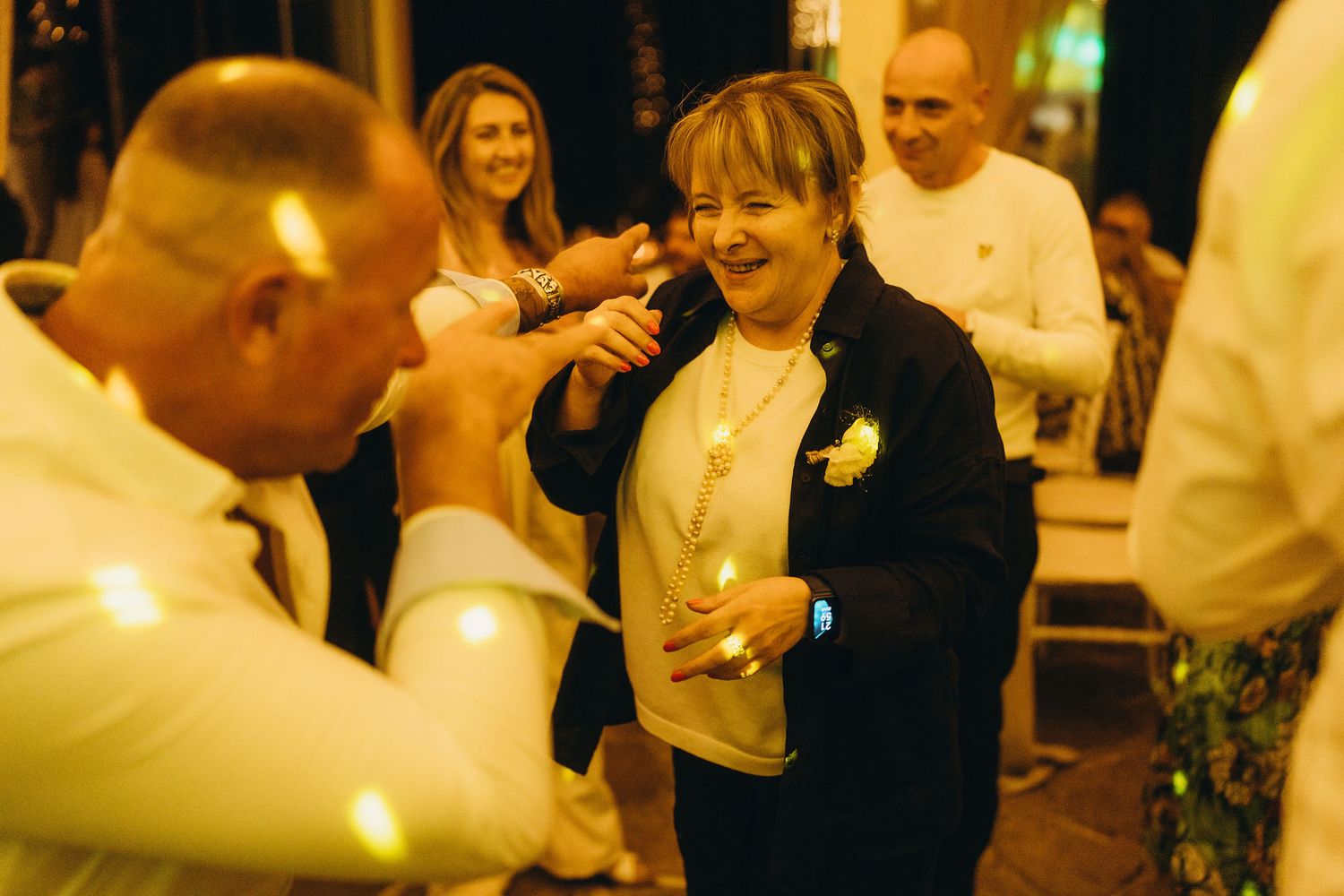 Woman in black jacket laughing and dancing at a festive evening wedding reception party.
