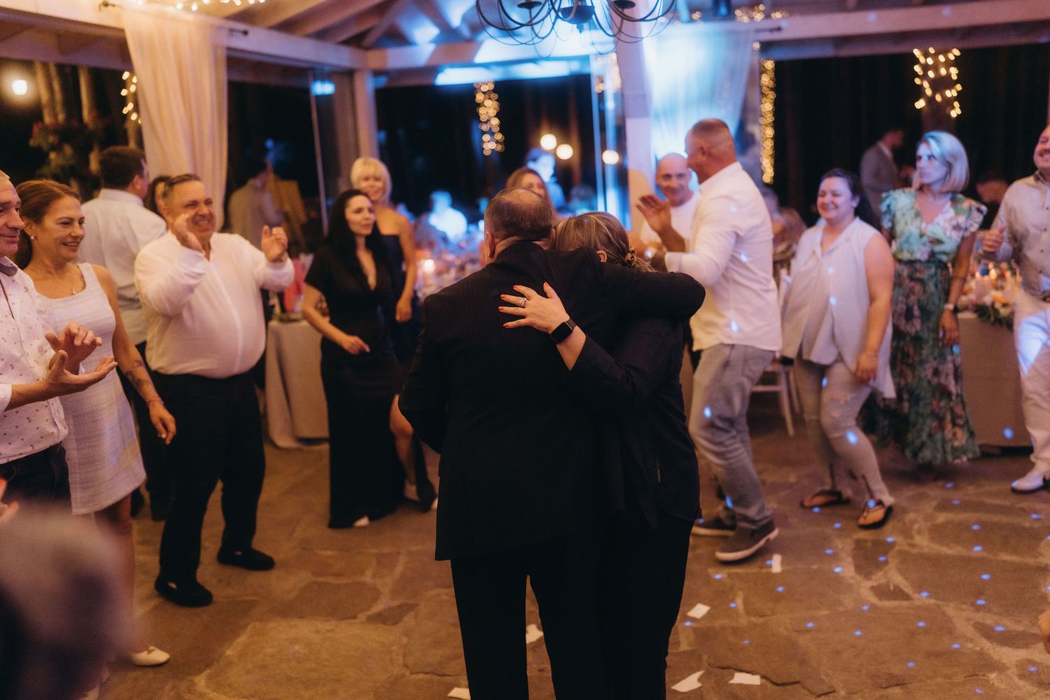 Guests hugging and dancing together on the floor at an elegant wedding reception celebration.