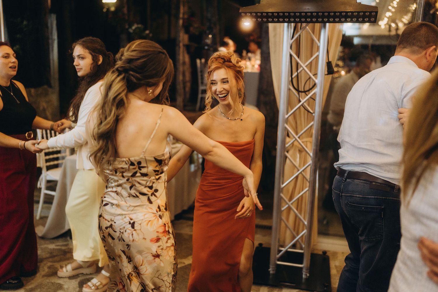Two women in elegant dresses dancing and laughing joyfully at a wedding reception party.