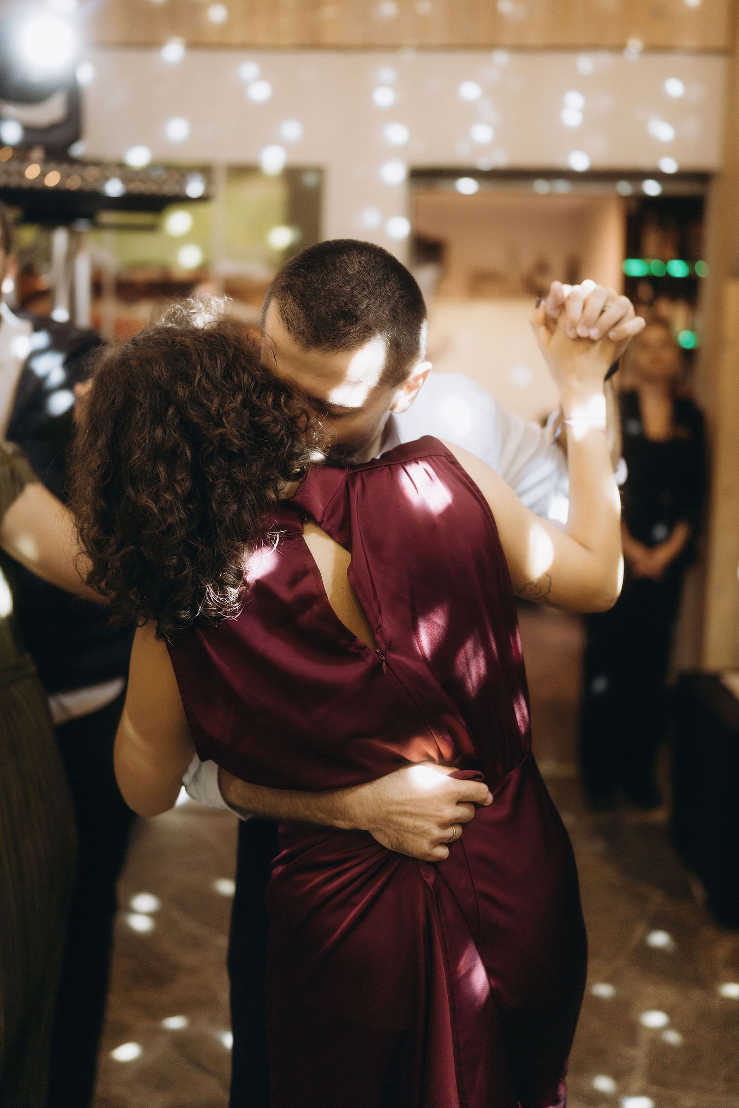 Couple sharing an intimate dance embrace in elegant evening wear at a romantic wedding reception with fairy lights.