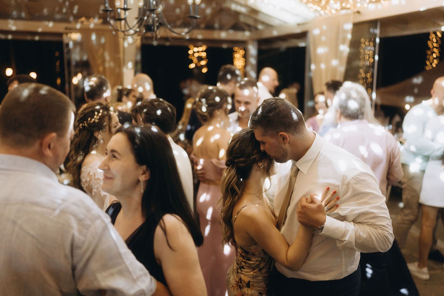 Couple shares intimate slow dance surrounded by guests and bubbles at romantic wedding reception.