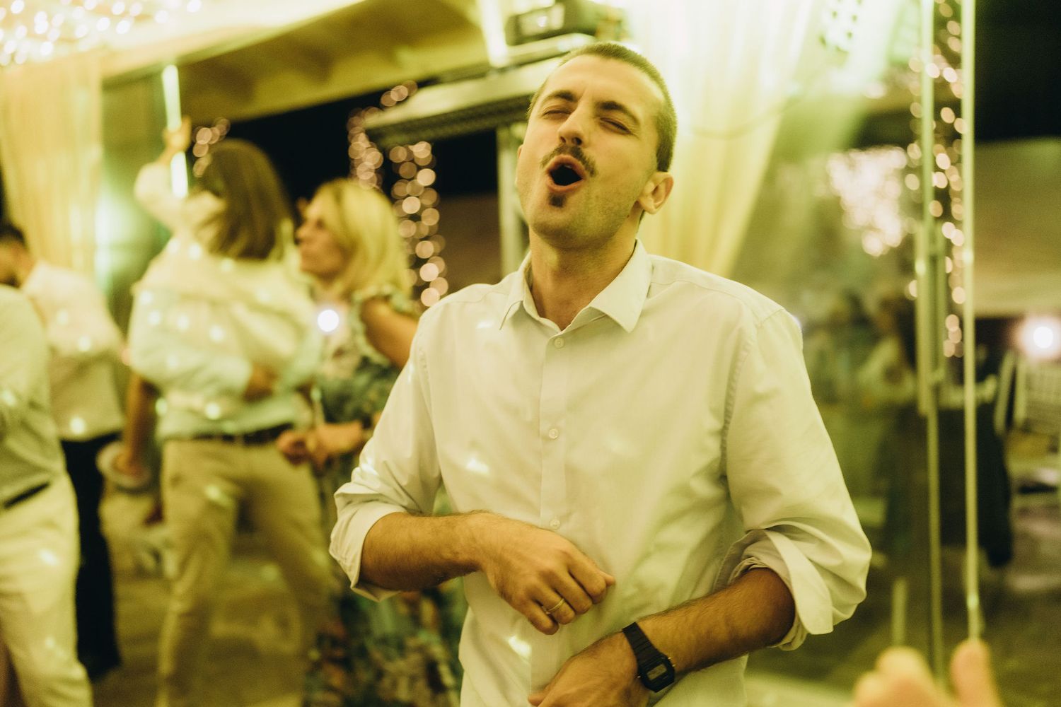 Enthusiastic man in white shirt sings and dances expressively at outdoor evening wedding celebration.