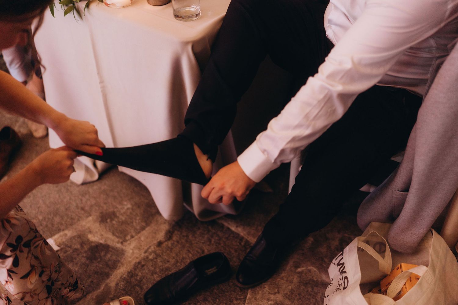 Groom adjusting his suit pants with assistance at a wedding preparation moment.