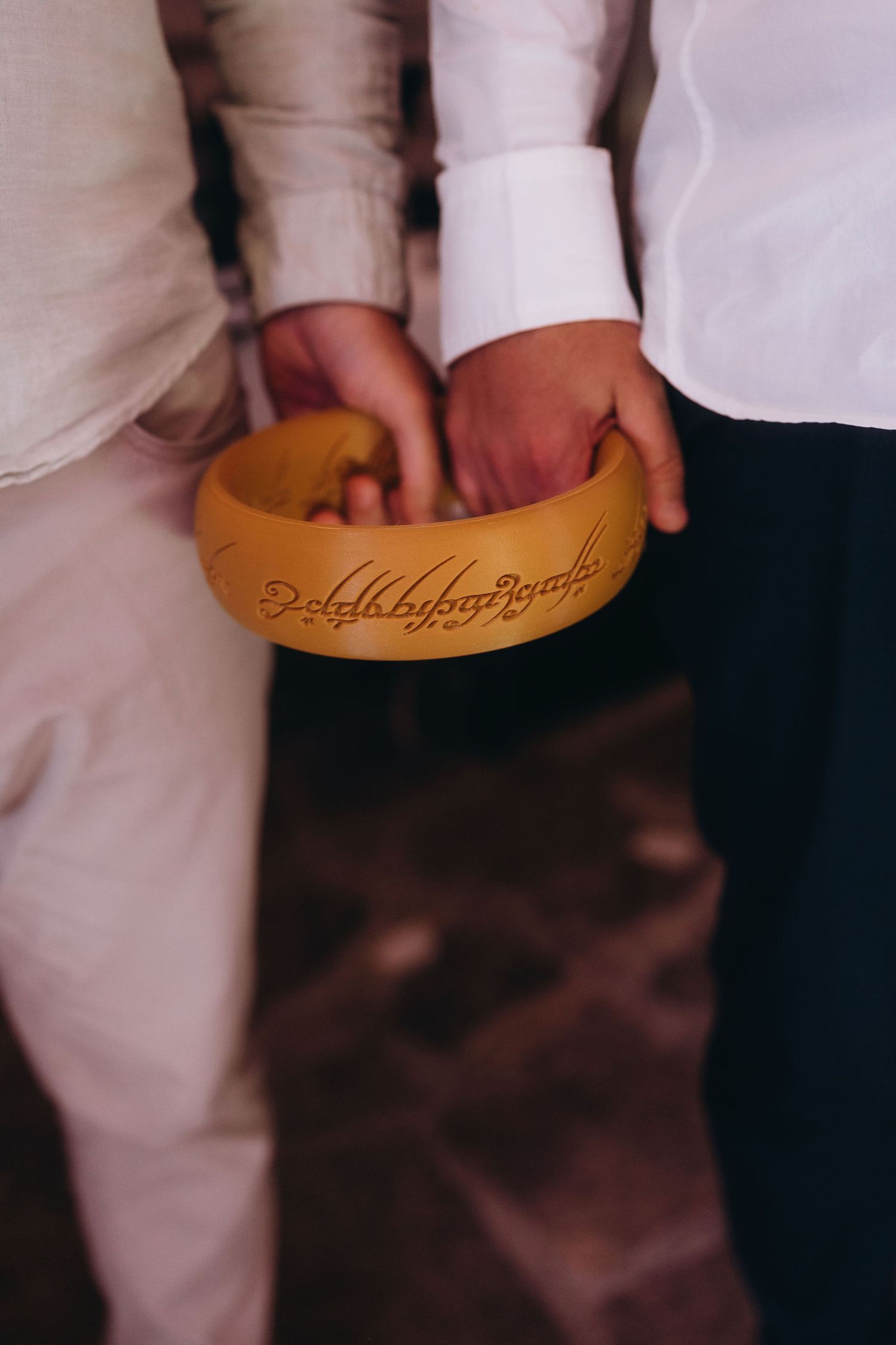Two people holding a golden wooden bowl engraved with Elvish script from Lord of the Rings at a wedding ceremony.