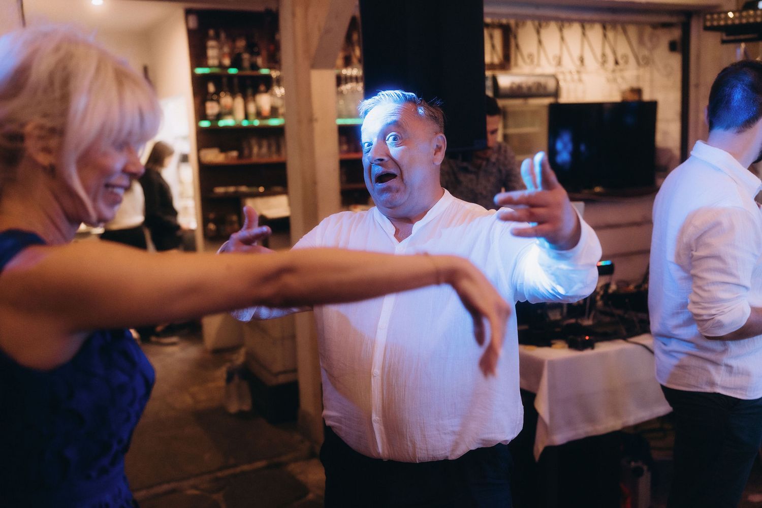 Guests dancing energetically at a lively indoor party or wedding reception with blue lighting.