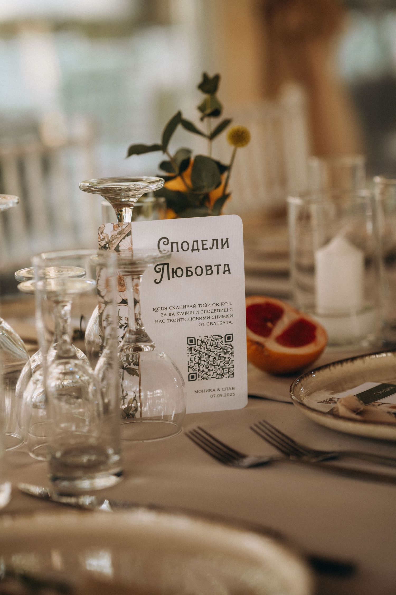 Elegant wedding table setting with QR code card reading Сподели Любовта, wine glasses, silverware, and grapefruit decor.