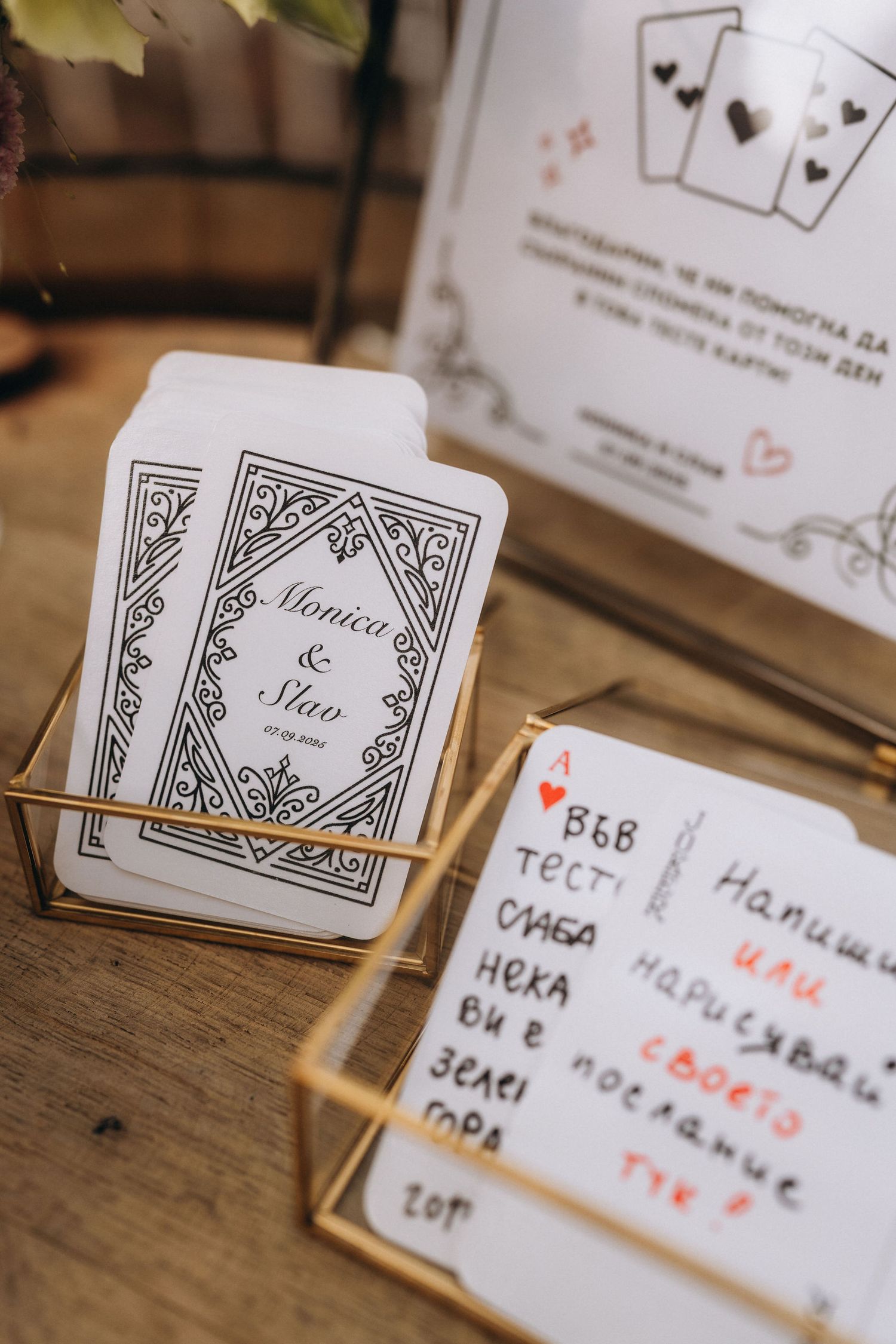 Wedding card box with personalized playing cards for Monica and Slav displayed in gold geometric holders on wooden table.