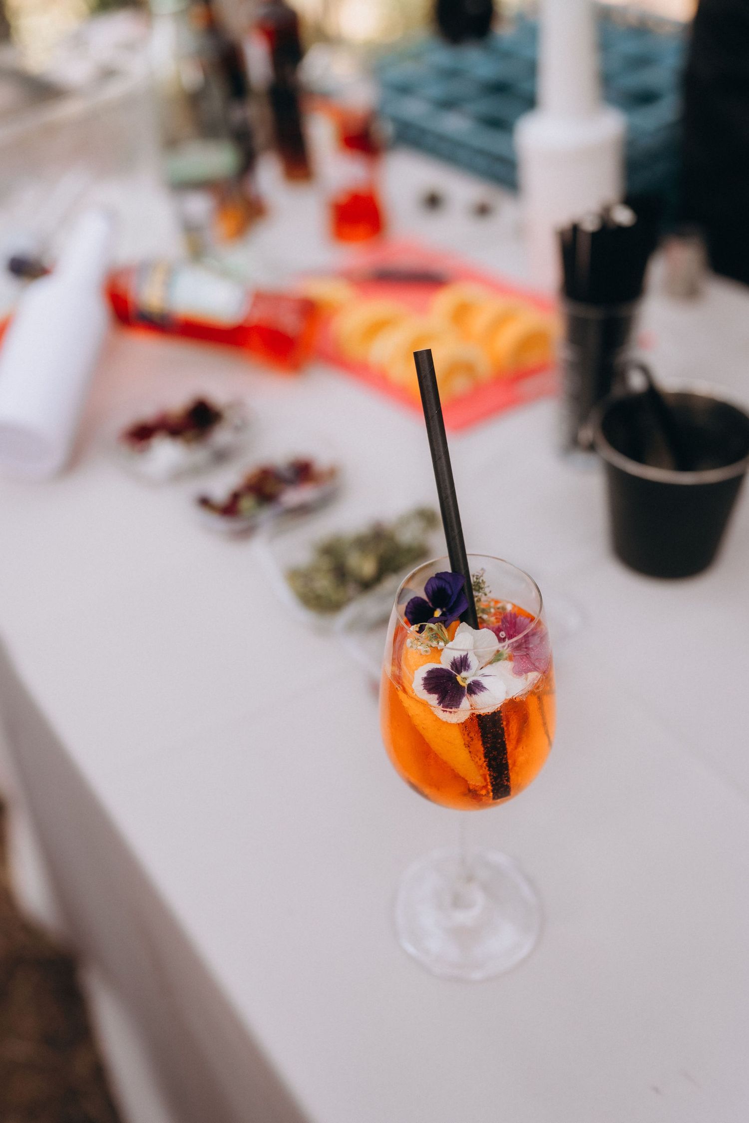 Elegant Aperol Spritz cocktail garnished with edible flowers and a black straw on a white bar counter.