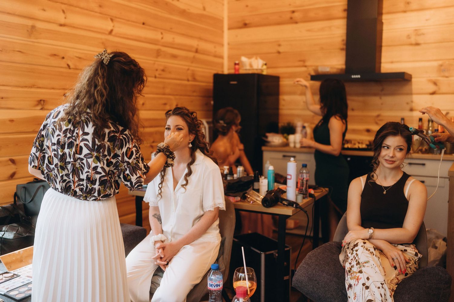 Women getting bridal hair and makeup done in a cozy wooden cabin before a wedding ceremony.