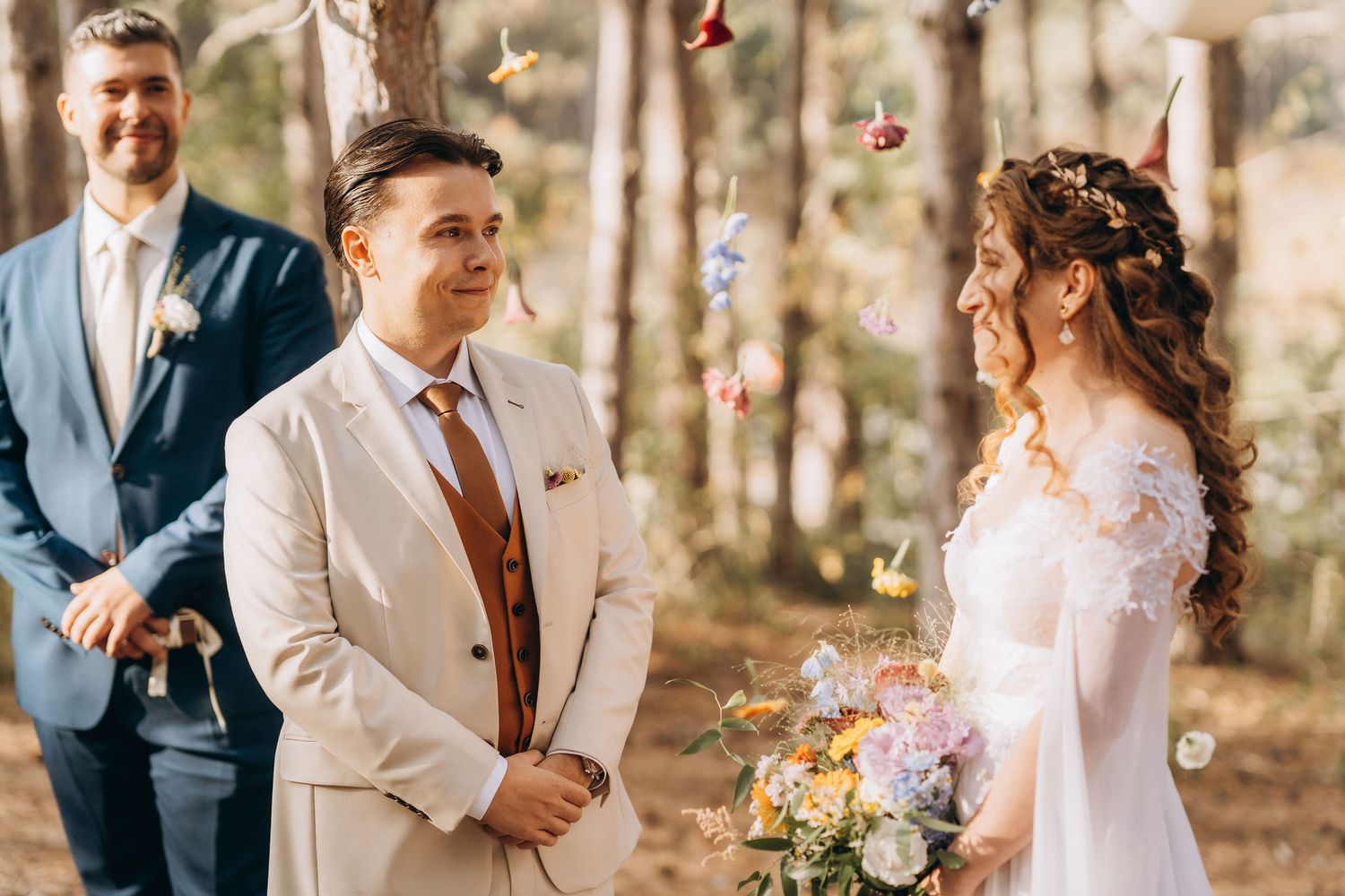 Outdoor woodland wedding ceremony with couple exchanging vows, bride holding colorful bouquet, colorful butterflies hanging in trees.