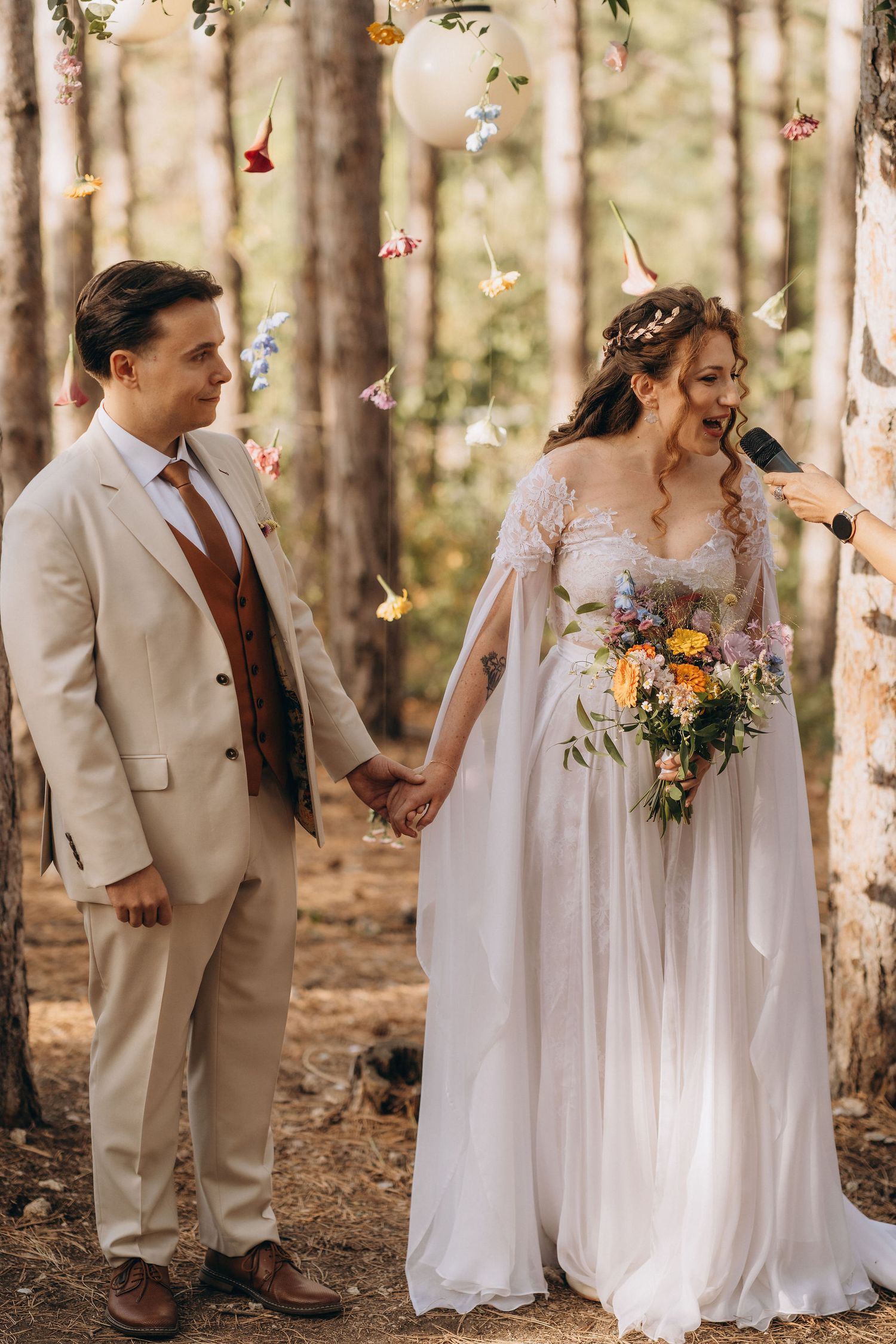 Bride and groom hold hands during outdoor forest wedding ceremony with colorful butterflies and paper lanterns.