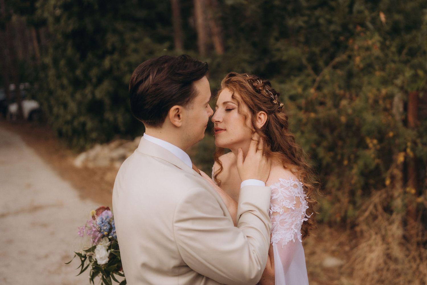 Groom tenderly touching bride's face during romantic outdoor forest wedding photo session.