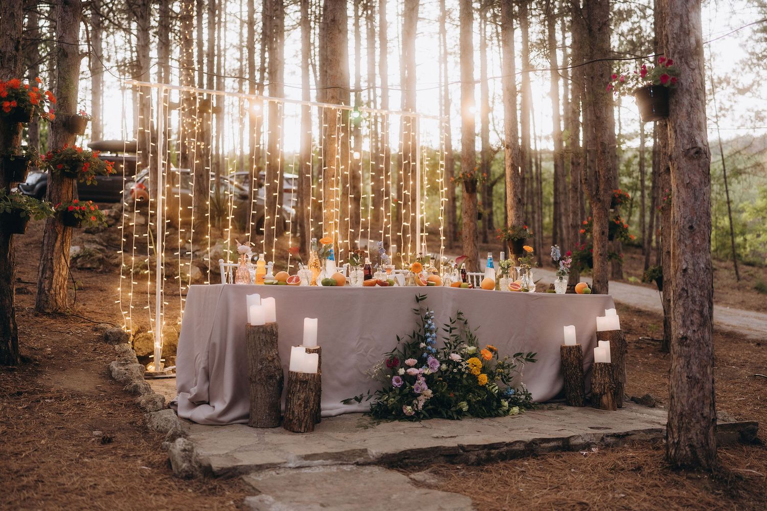 Enchanting outdoor wedding reception table with fairy lights hanging between trees in a forest setting.