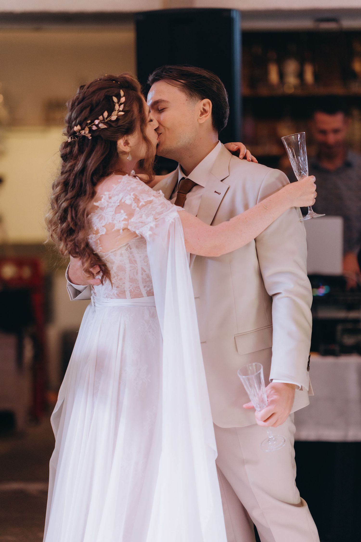 Bride and groom share a first kiss while holding champagne glasses at their indoor wedding reception.