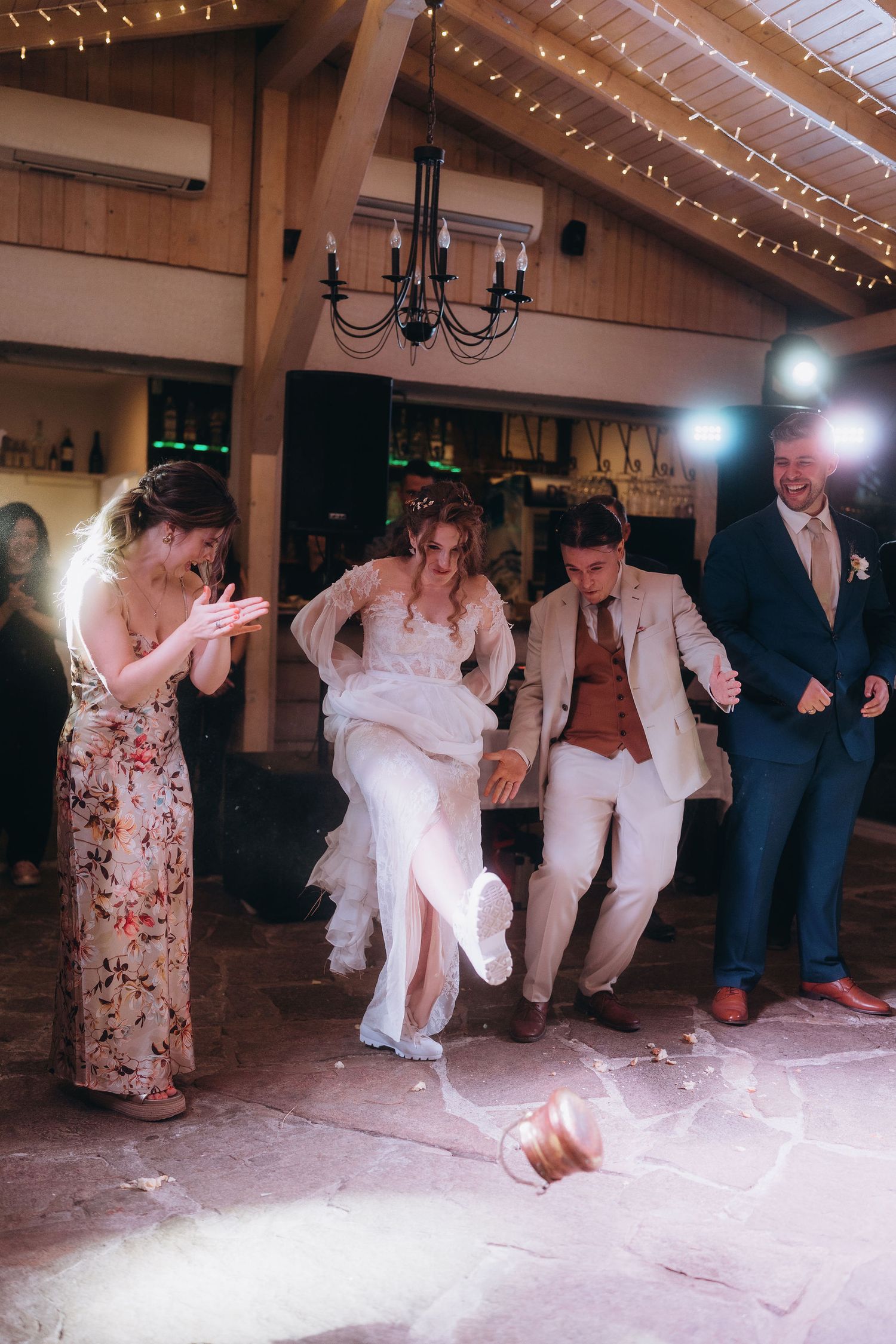 Bride and groom joyfully jump together on the dance floor surrounded by wedding guests during reception celebration.