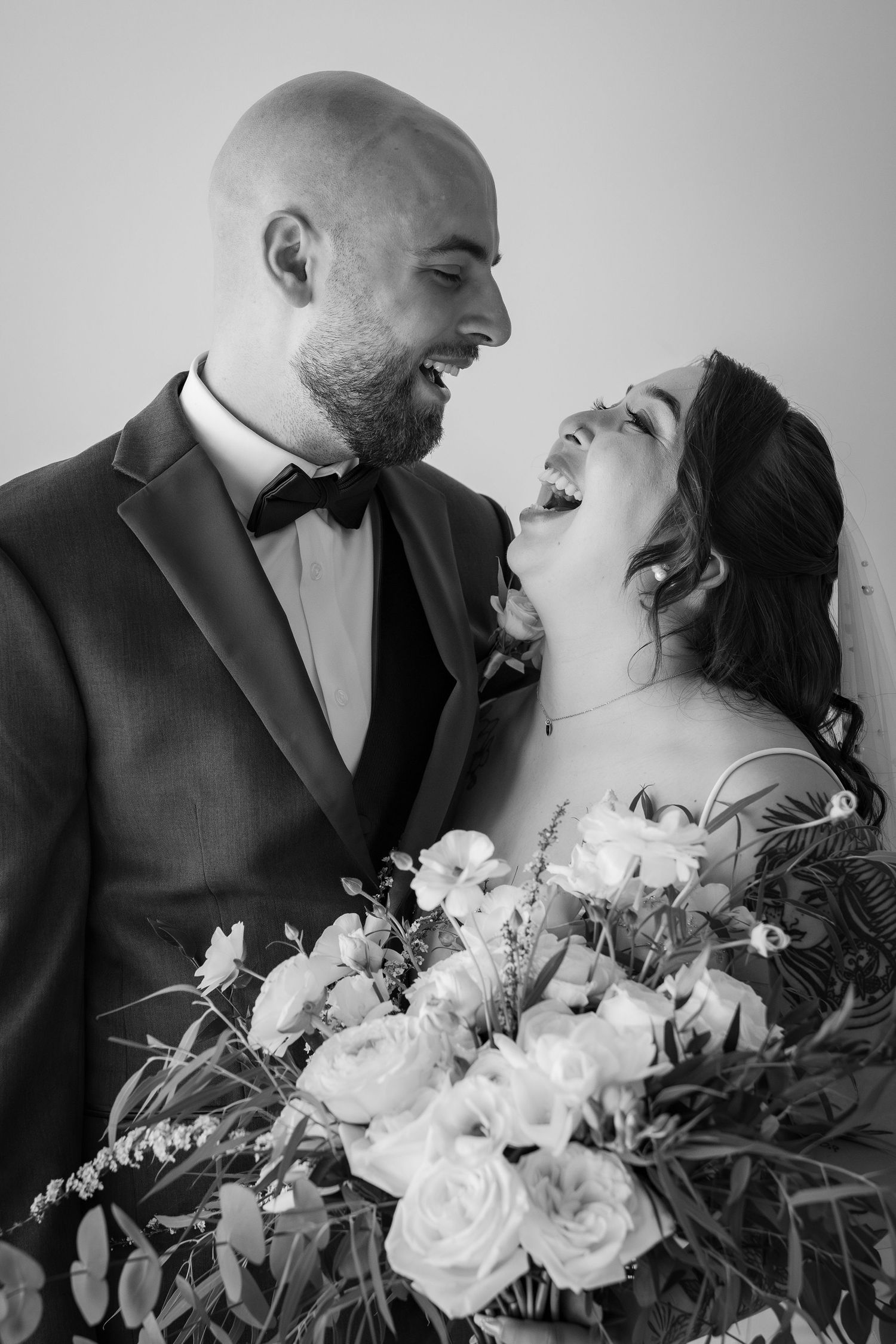 Black and white photo of laughing bride and groom with wedding bouquet.