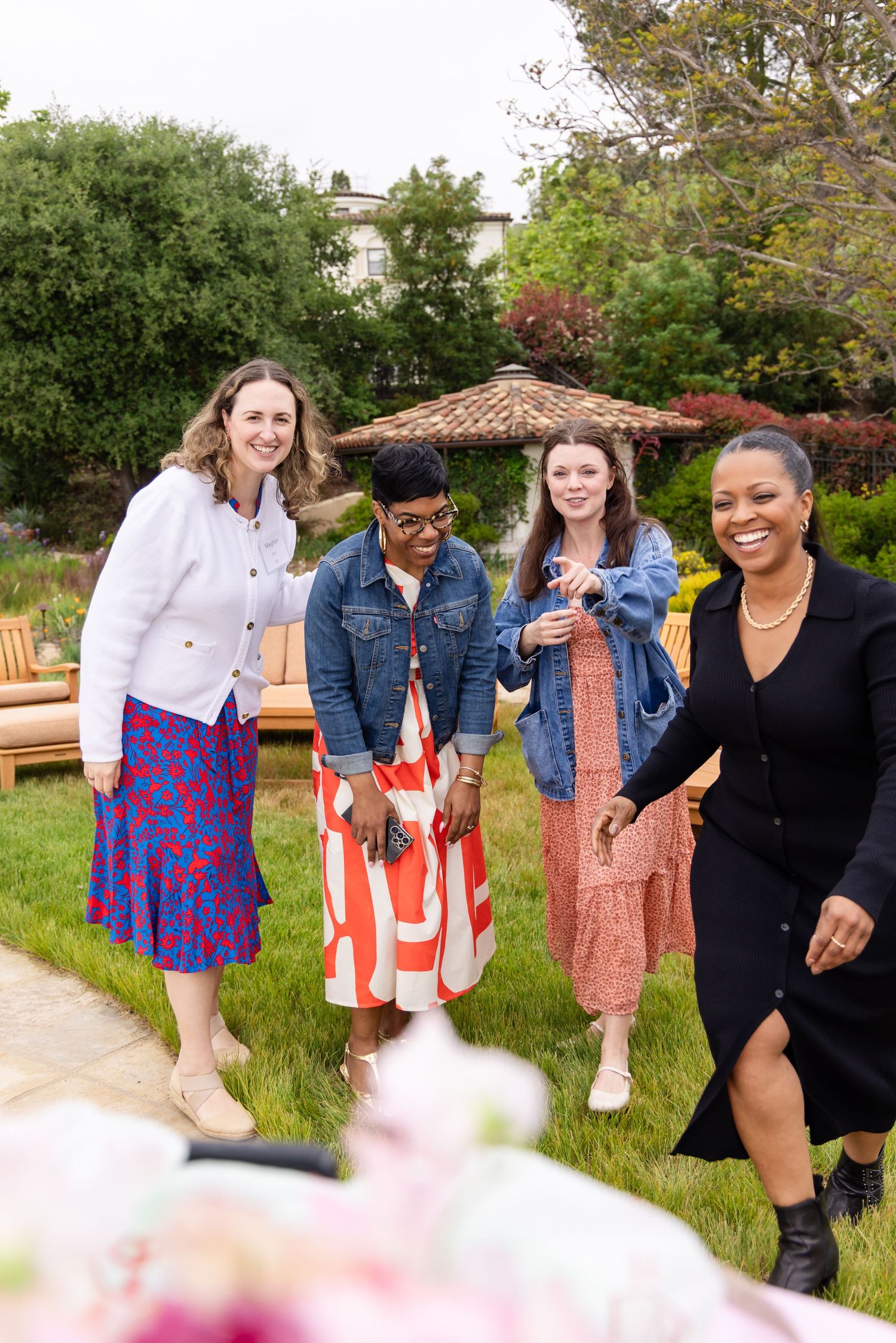 Four women smiling and posing together in a lush garden at an outdoor event.