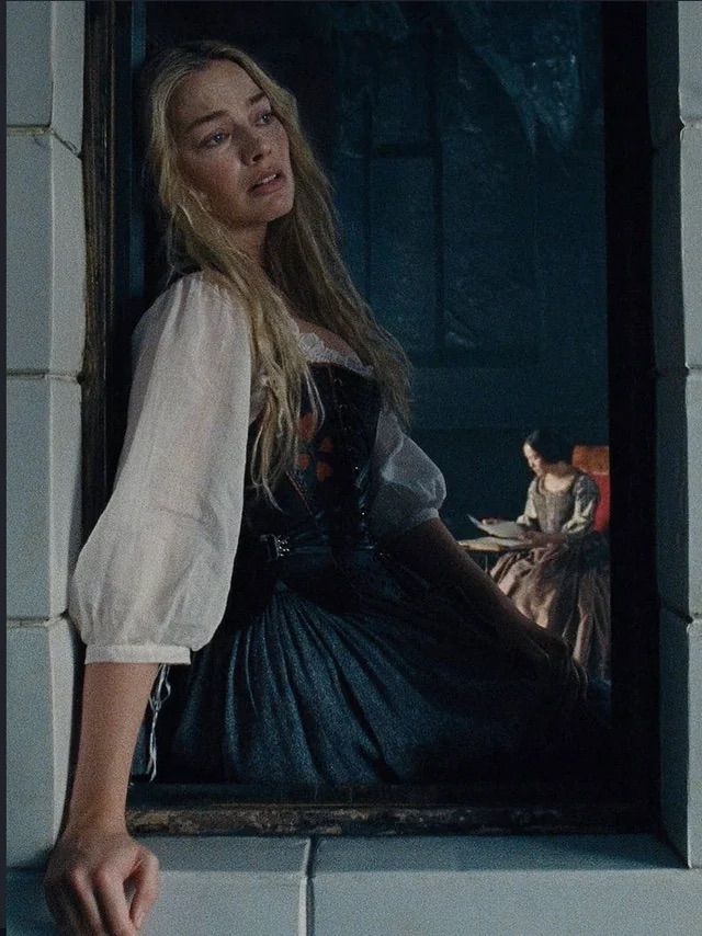 Young woman in period costume with white blouse and dark corset sits in a stone window frame.