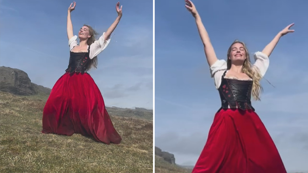 Woman in red skirt and black corset dances joyfully on scenic highland landscape.