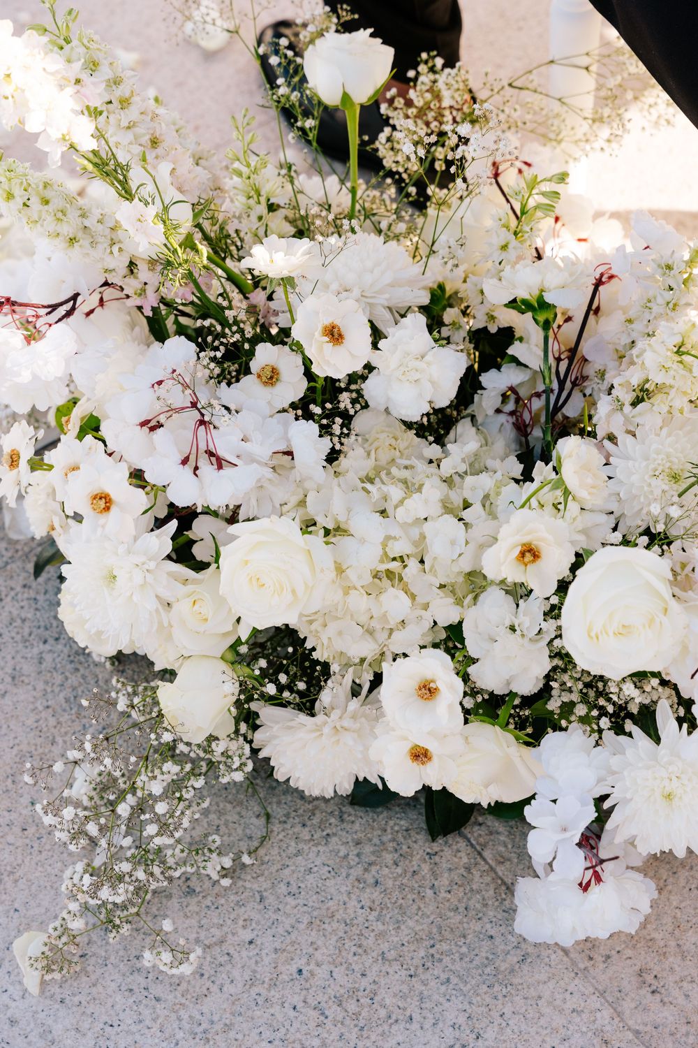 Lush white wedding floral arrangement featuring roses, baby's breath, and mixed blooms on a marble floor.