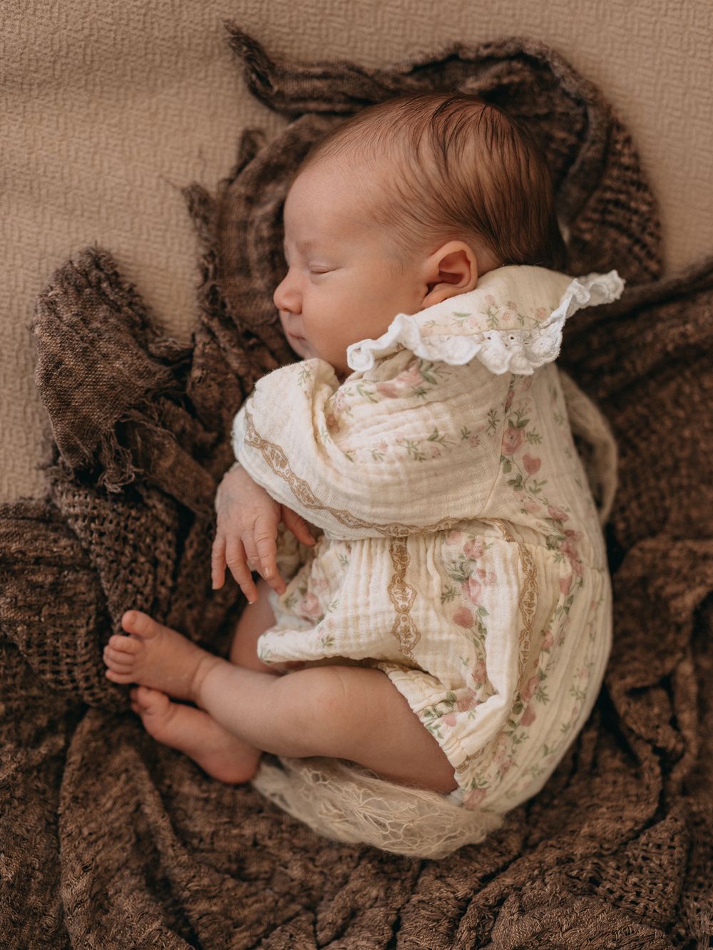 Peaceful newborn baby sleeping in vintage floral romper on brown knit blanket.