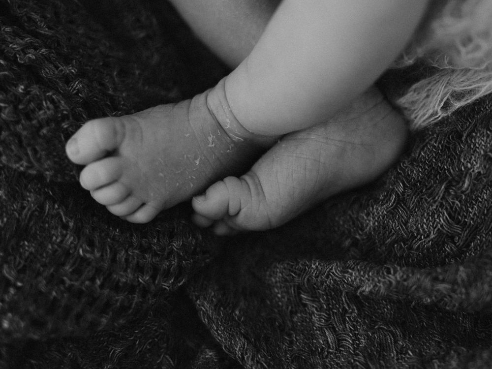 Black and white close-up photo of tiny newborn baby feet resting on a soft knit blanket.