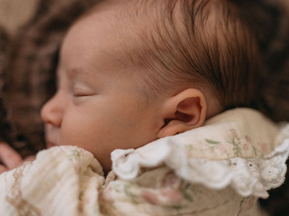 Peaceful newborn baby sleeping wrapped in a delicate floral lace blanket, close-up portrait photography.