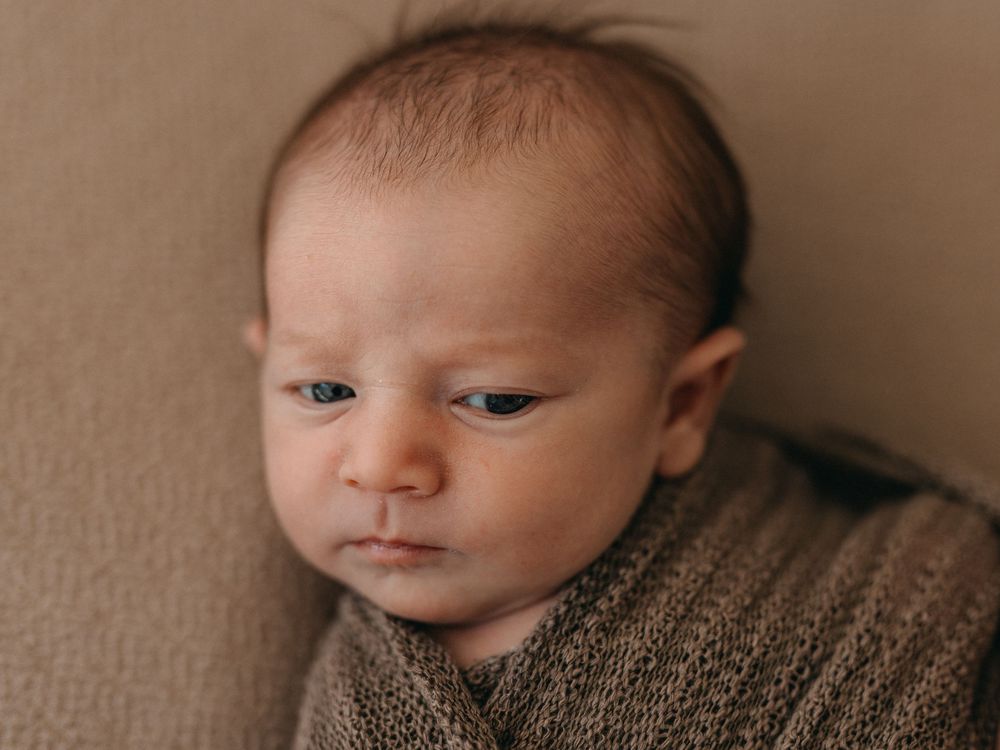 Close-up portrait of a peaceful newborn baby wrapped in a soft brown knit blanket with delicate features.