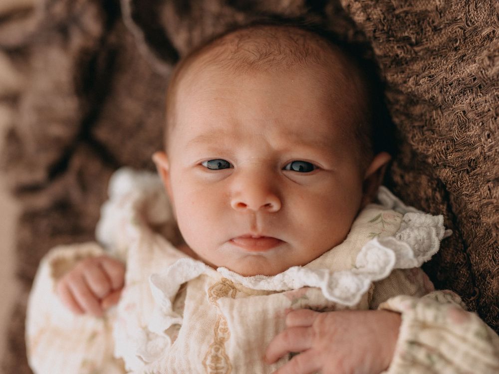 Newborn baby in vintage lace gown lying on brown fur, with blue eyes and a serious expression.