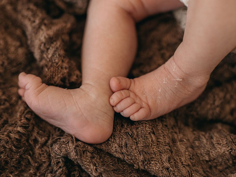 Close-up of tiny newborn baby feet resting on a soft brown knit blanket.