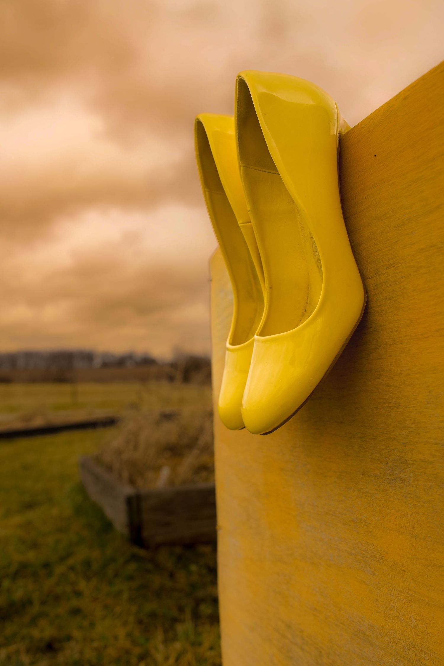 Yellow high heel shoes balanced on a golden pillar outdoors under a dramatic cloudy sky.
