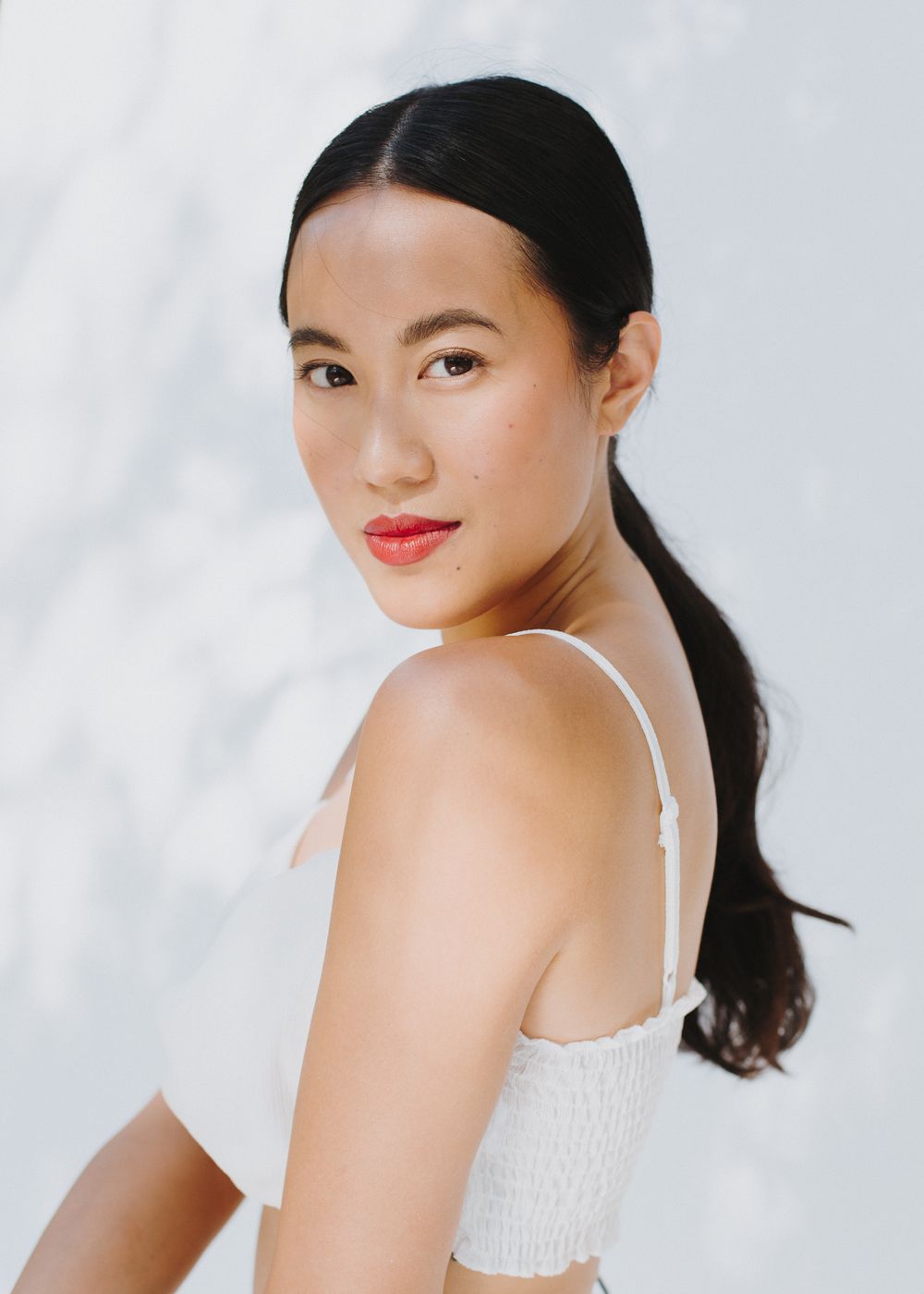 Asian model in white top poses against light background in series of headshots.
