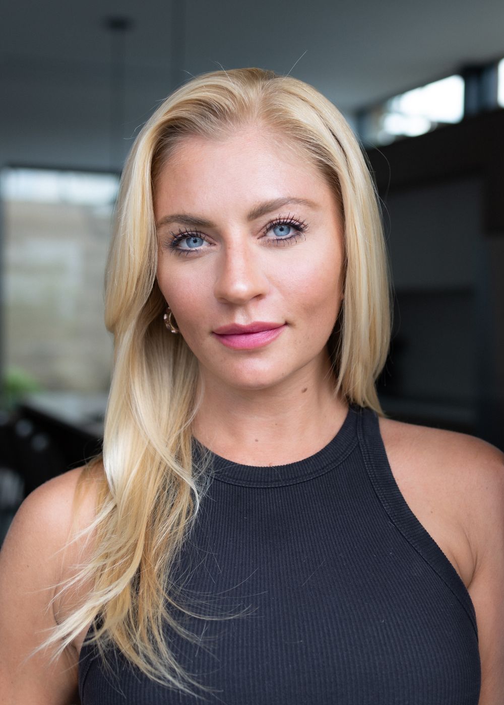 A close-up portrait shot against a dark background wearing a black sleeveless top.