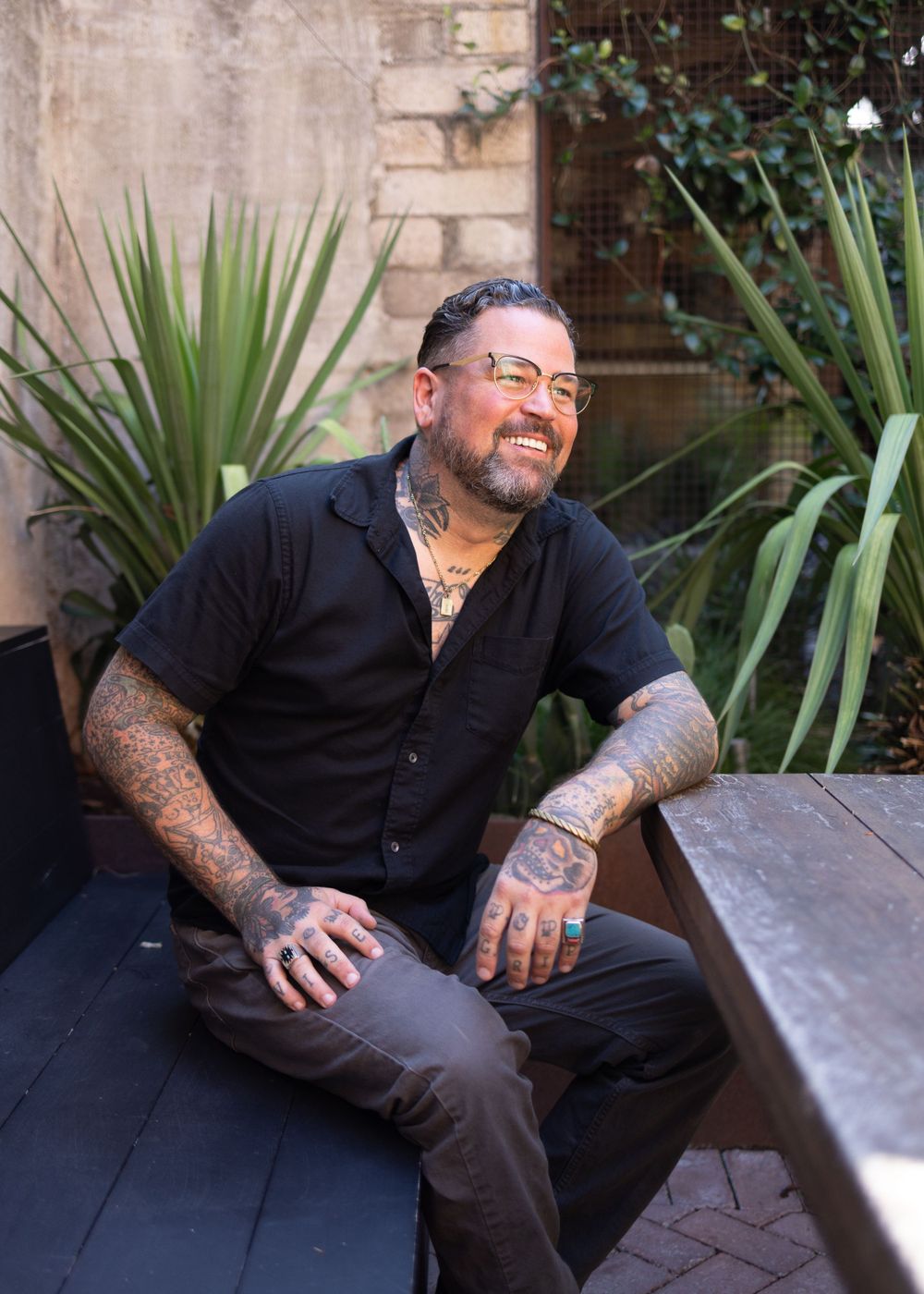 Casual outdoor portrait series of man in black shirt showing tattoos and genuine smiles.