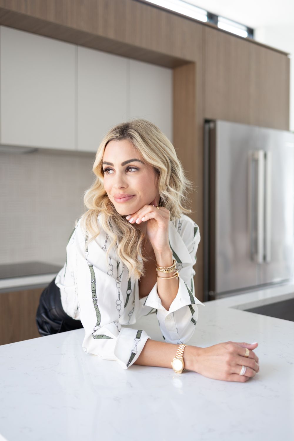Elegant portrait of person in white blouse leaning on white counter in modern kitchen.