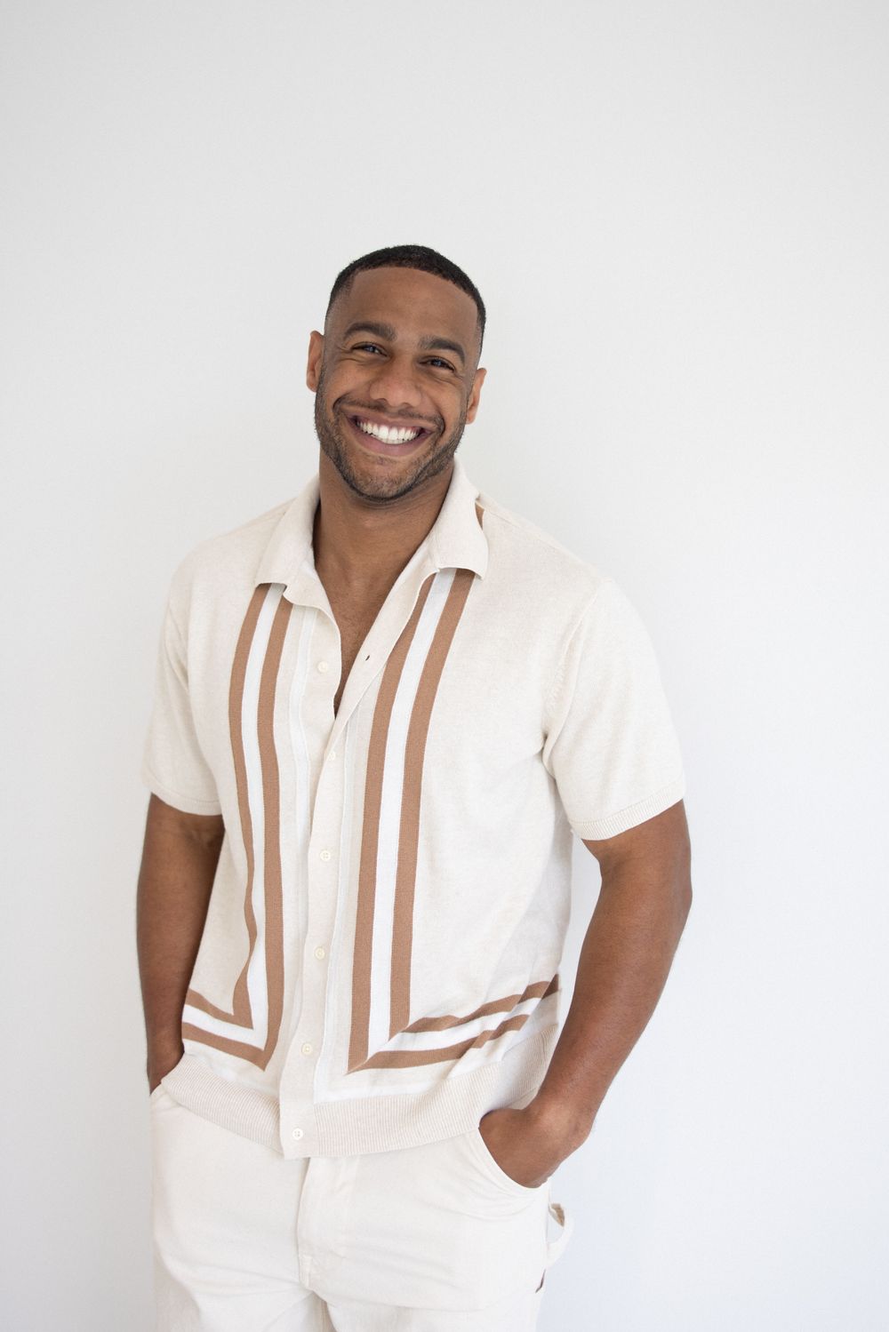 Stylish portrait of person wearing cream colored shirt with brown stripes against white background.