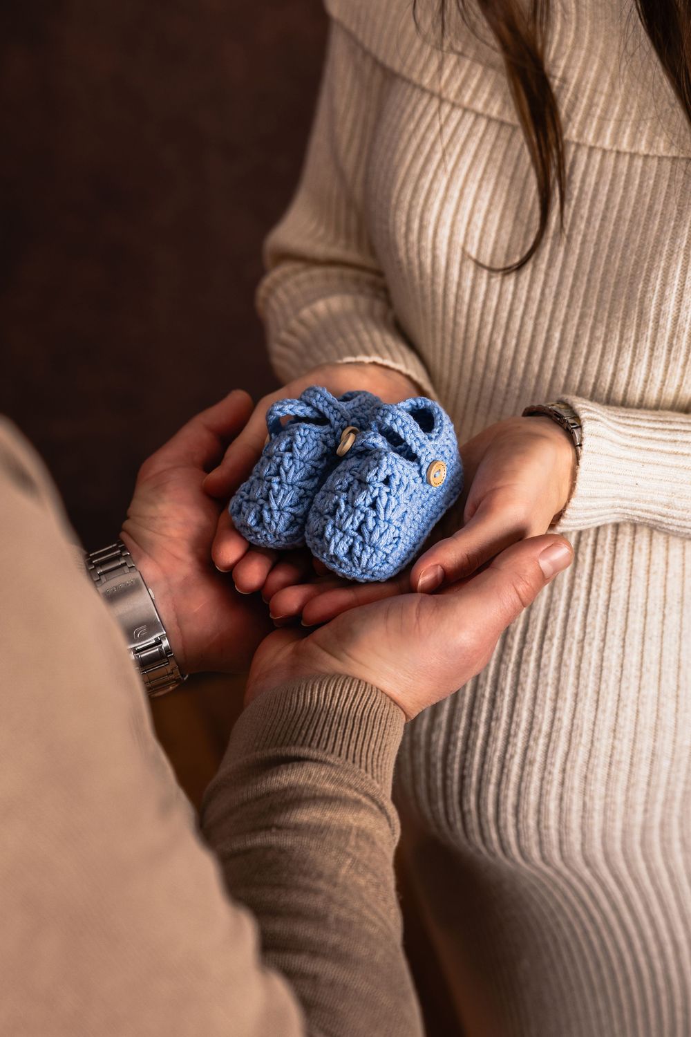 kismama és férje tartják a kiscipőket kezükben egy közeli részletfotón