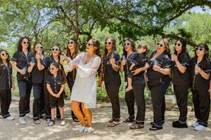 Wedding party group photo with coordinated black outfits and sunglasses posing outdoors.