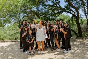 Fun group photo of wedding party in matching black outfits posing casually outdoors.
